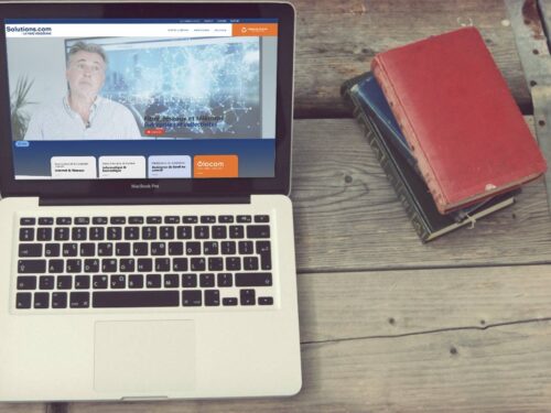 Ordinateur portable à côté d'un agenda rouge présentant la création du site internet de Vendée Solutions